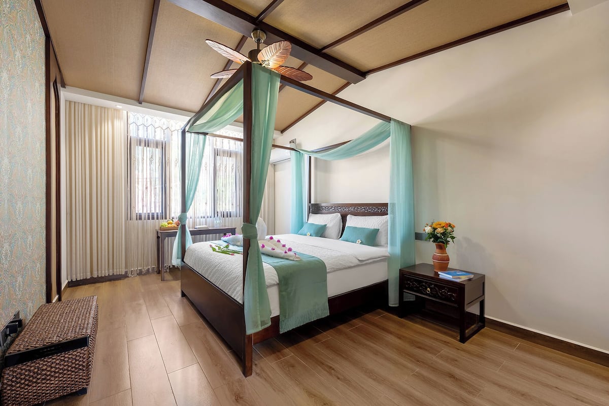 A four-poster bed with a canopy, a bedside table with a vase of flowers, and a wooden bench.