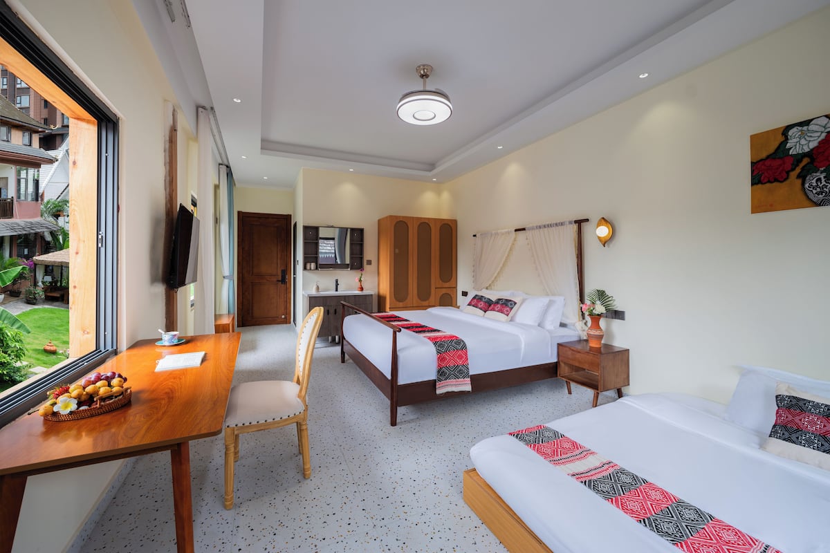 A hotel room with a bed, bedside table, chair, and a desk with a basket of fruit.