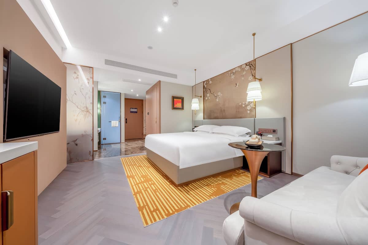 A modern hotel room with a large bed, a desk, a TV, and a seating area.