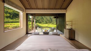 A bedroom with a large bed, a view of a lush green landscape, a small table with fruit, and a seating area with chairs. - Country Retreats Zhangjiajie Manson Resort (Zhangjiajie)