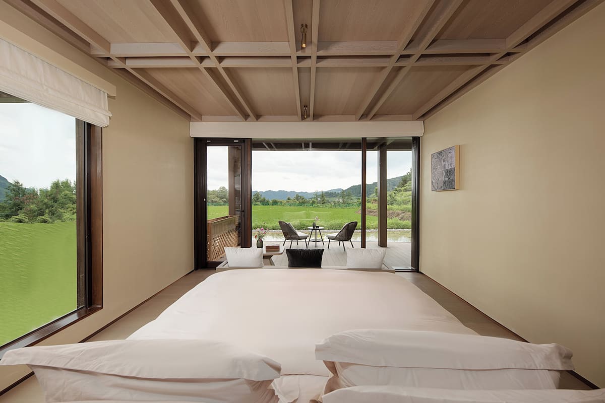 Une chambre avec un grand lit, une vue sur un paysage verdoyant et une petite table avec des chaises.