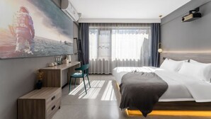Habitación de hotel moderna con una cama grande, un escritorio, una silla y un ventanal con cortinas.