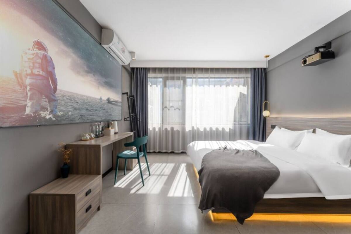 Habitación de hotel moderna con una cama grande, un escritorio, una silla y un ventanal con cortinas.