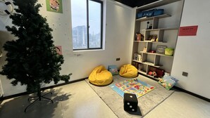 Una habitación con un árbol de Navidad, sillones de mimbre, una alfombra, una estantería y una ventana con vistas a la ciudad.