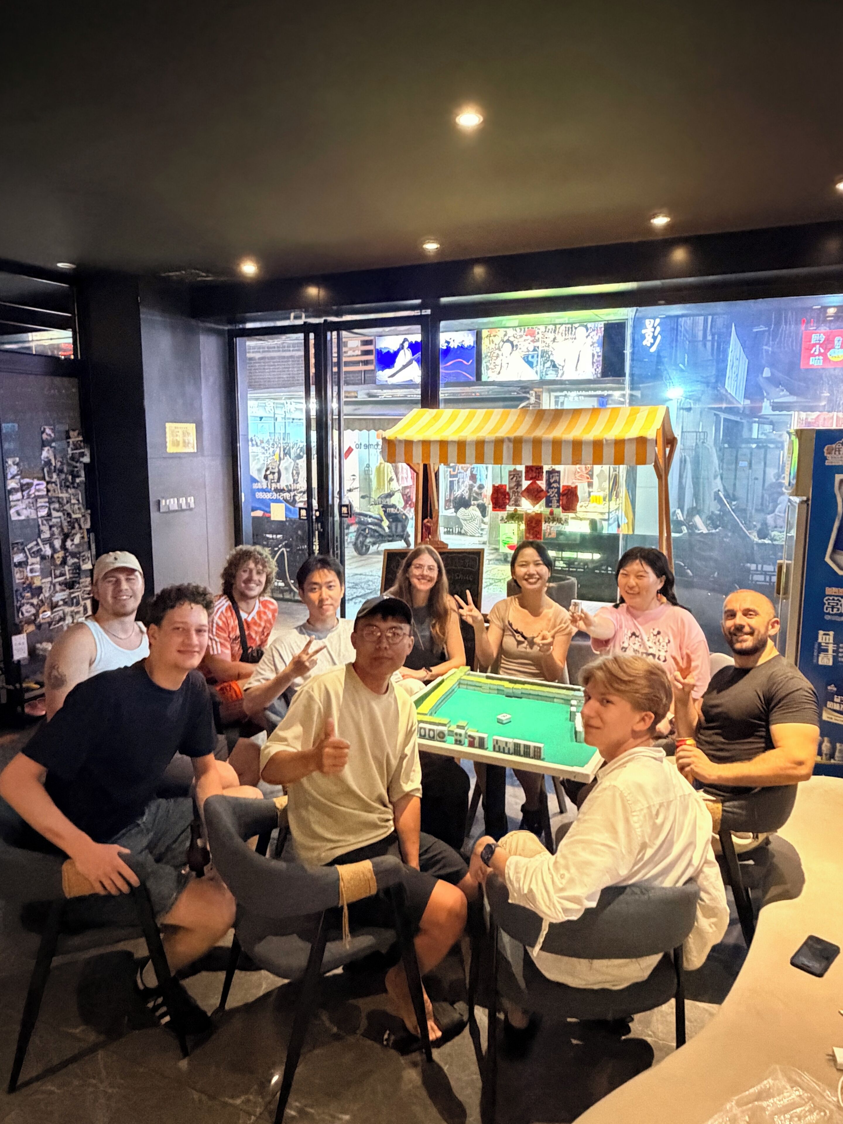 A group of people seated around a pool table in a room with large windows and a cityscape view.