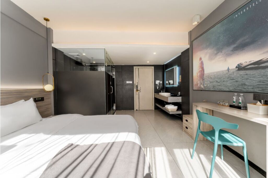 Habitación de hotel moderna con una cama grande, un baño con cabina de ducha de vidrio, un tocador con espejo y un ventanal con vista al mar.