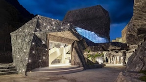 Un edificio moderno con una estructura singular que recuerda a una roca, una escalera y un frente de vidrio.