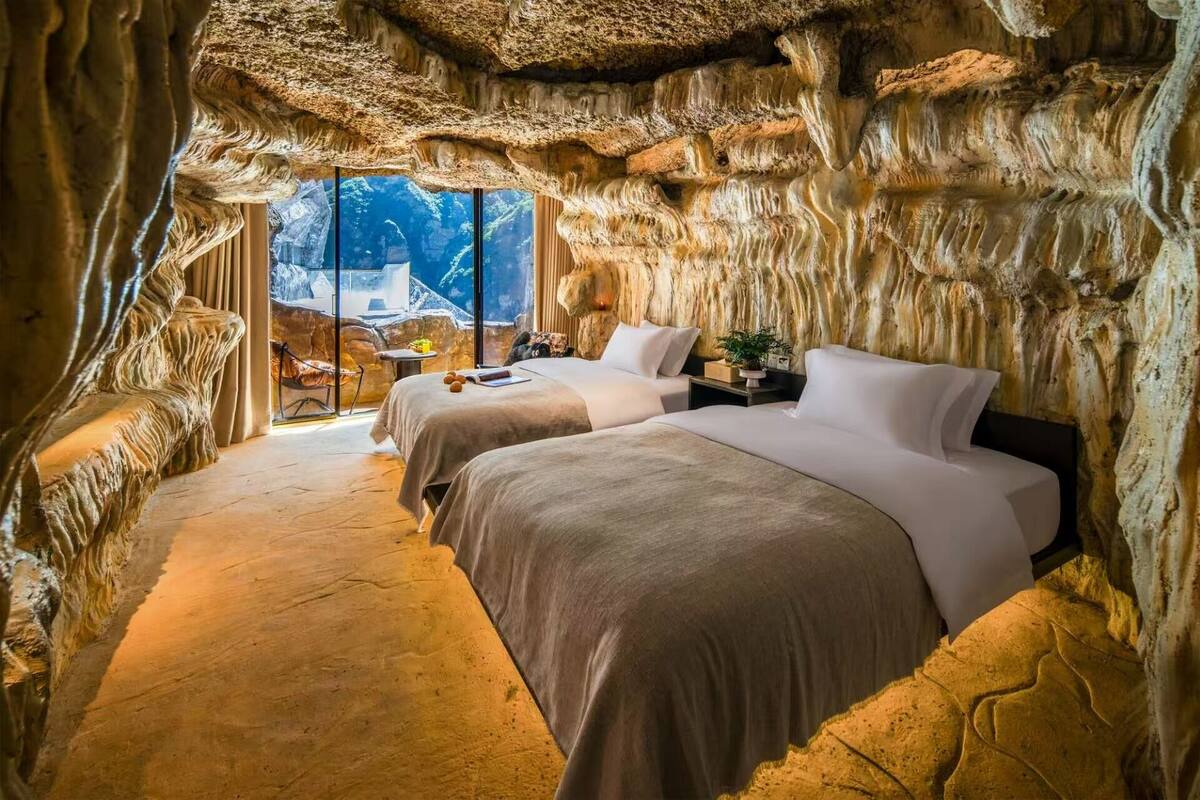 Um quarto tipo caverna com duas camas, uma mesa pequena e vista para o exterior.