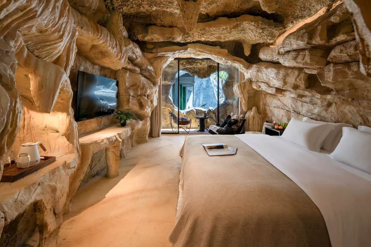 Um quarto tipo caverna com uma cama, uma televisão e vista para uma cascata.