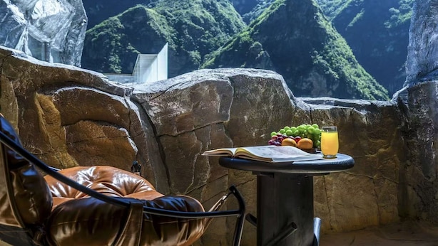 Un muro de piedra con una mesa, una silla, un libro y un frutero con una bebida.