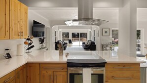 Une cuisine moderne avec des meubles en bois, une hotte de cuisine en acier inoxydable et un îlot central doté d’un four encastré.