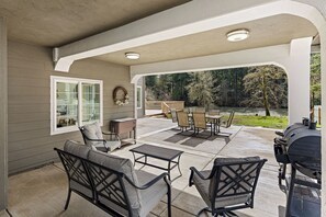A covered patio with outdoor furniture, a grill, and a view of a wooded area. - River's Rest: 3BR, waterfront views, hot tub, grill, fire pit! (Walterville)