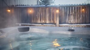 A hot tub with a wooden deck and a metal railing in a snowy outdoor setting.