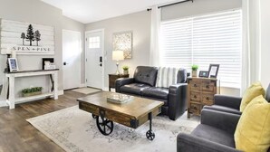 A modern living room with a leather sofa, a coffee table with wheels, a wooden console table, and a large window with blinds.