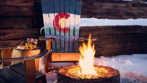 A wooden cabin with a fire pit and a painted Adirondack chair.