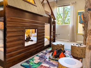 Acogedora habitación tipo cabaña con literas, una ventana pequeña y un tronco de árbol como elemento decorativo en la pared.
