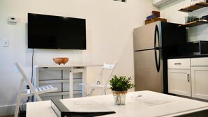 Eine moderne Küche mit weißen Schränken, einem schwarzen Kühlschrank, einer Mikrowelle und einem wandmontierten Flachbildfernseher.
