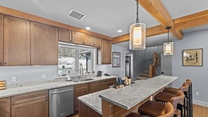 A modern kitchen with wooden cabinets, granite countertops, and a bar area with leather stools.
