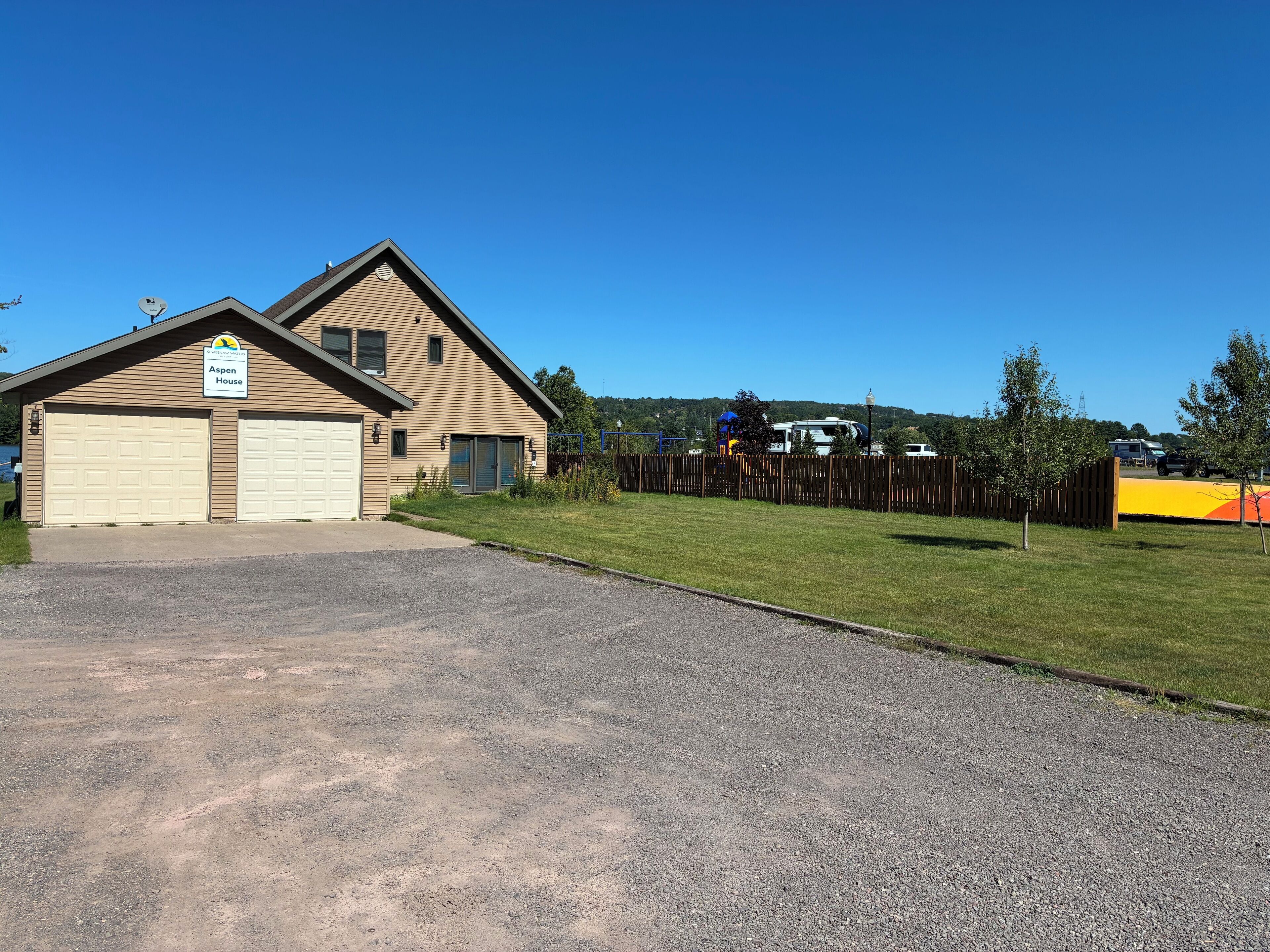 A two-story house with a garage, a fenced yard, and a clear blue sky.