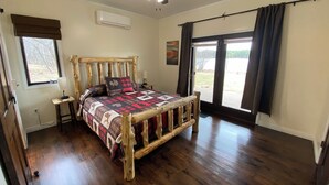 Un dormitorio con cama de madera, ventilador de techo, ventana con cortinas y vistas al exterior.