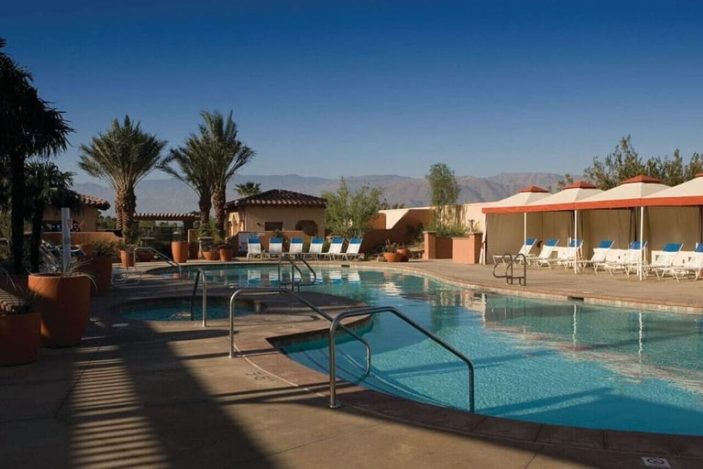 A pool area with lounge chairs, palm trees, and a mountain backdrop.