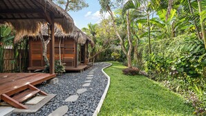 A tropical resort with thatched-roof cabins, a stone pathway, and lush greenery. - Satvik Hut Villa by Betterplace (Kerobokan)