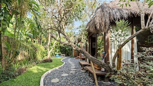 A garden pathway leading to a thatched-roof structure with outdoor seating. - Satvik Hut Villa by Betterplace (Kerobokan)
