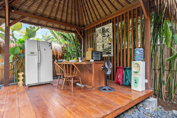 Una terraza de madera con un refrigerador, un ventilador, un dispensador de agua y una mesa con sillas.