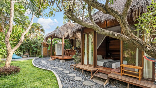 A tropical resort with thatched-roof cabins, a stone pathway, and lush greenery. - Satvik Hut Villa by Betterplace (Kerobokan)