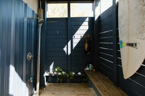A narrow entryway with a wooden bench, a surfboard, and a small shelf with bottles. - Studio Orange (Wilmington)
