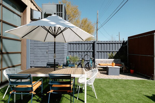 A patio with a table and chairs, a white umbrella, and a wooden fence. - Studio Orange (Wilmington)