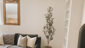 Un soggiorno con un divano scuro, una pianta in vaso, uno specchio con cornice in legno e una stufa a legna nera.