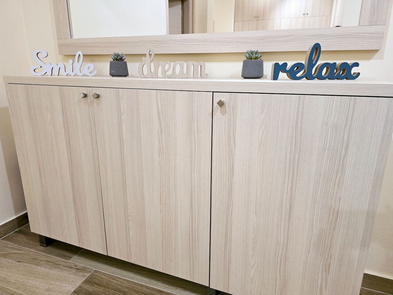 A wooden cabinet with a mirror above it and decorative words on the top.