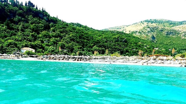 Une zone côtière dotée d’une plage, d’une eau turquoise et limpide, et d’un paysage de collines verdoyantes en arrière-plan.