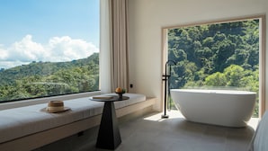 A modern bathroom with a large bathtub, a window seat with a hat and book, and a view of a forested hillside. - Miyue Shenzhen Tianlu Secret Wild Wizard Holiday Hotel (Shenzhen)