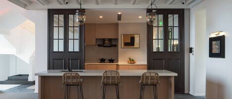 A modern kitchen with a central island, bar stools, pendant lighting, and a view of the adjacent living area.