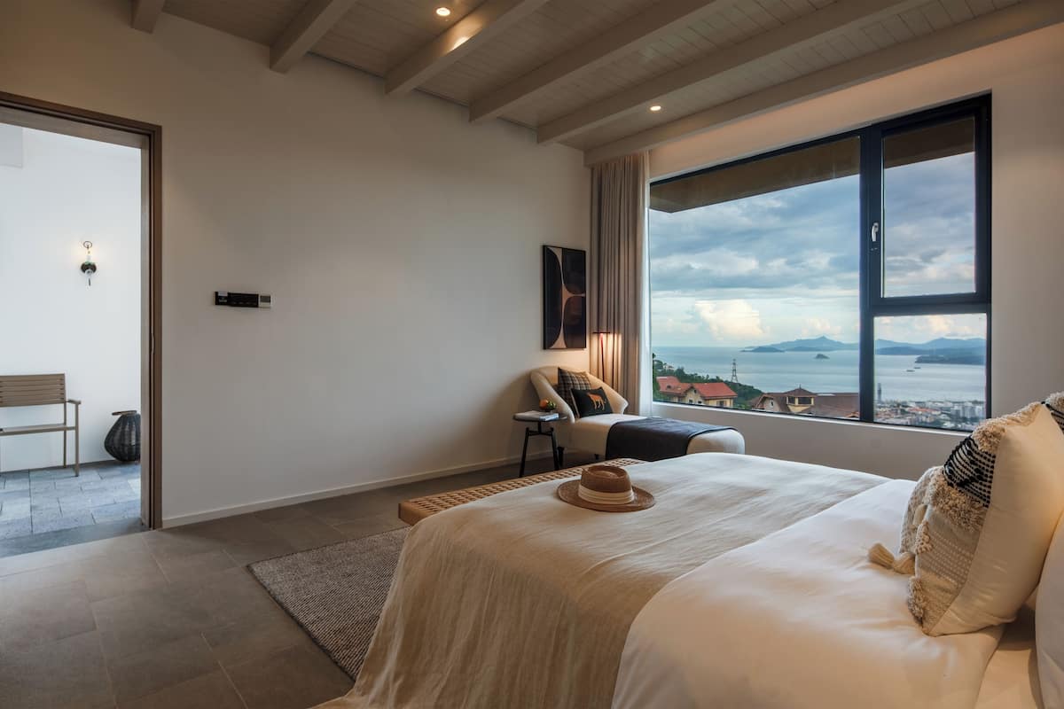 A modern bedroom with a large bed, a view of the sea, and a balcony.