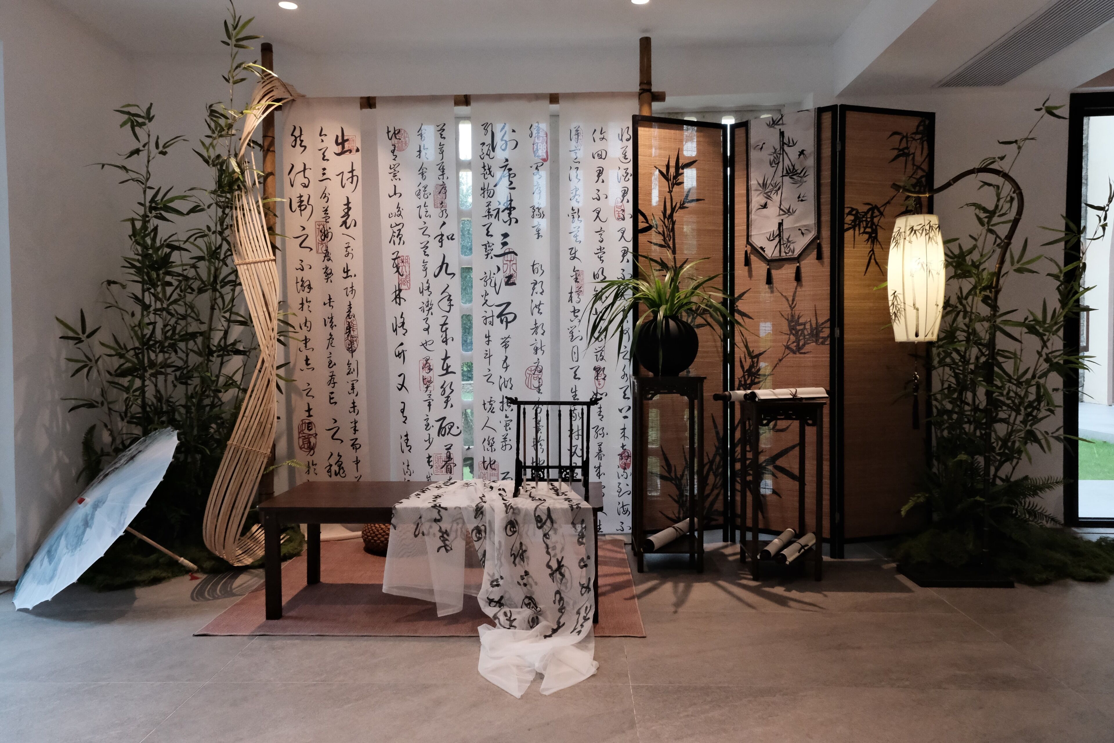 A traditional Japanese room with tatami flooring, a low table, a hanging lamp, and bamboo plants.