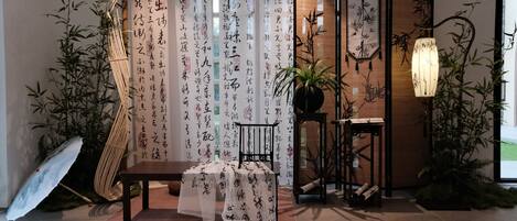A traditional Japanese room with tatami flooring, a low table, a hanging lamp, and bamboo plants.