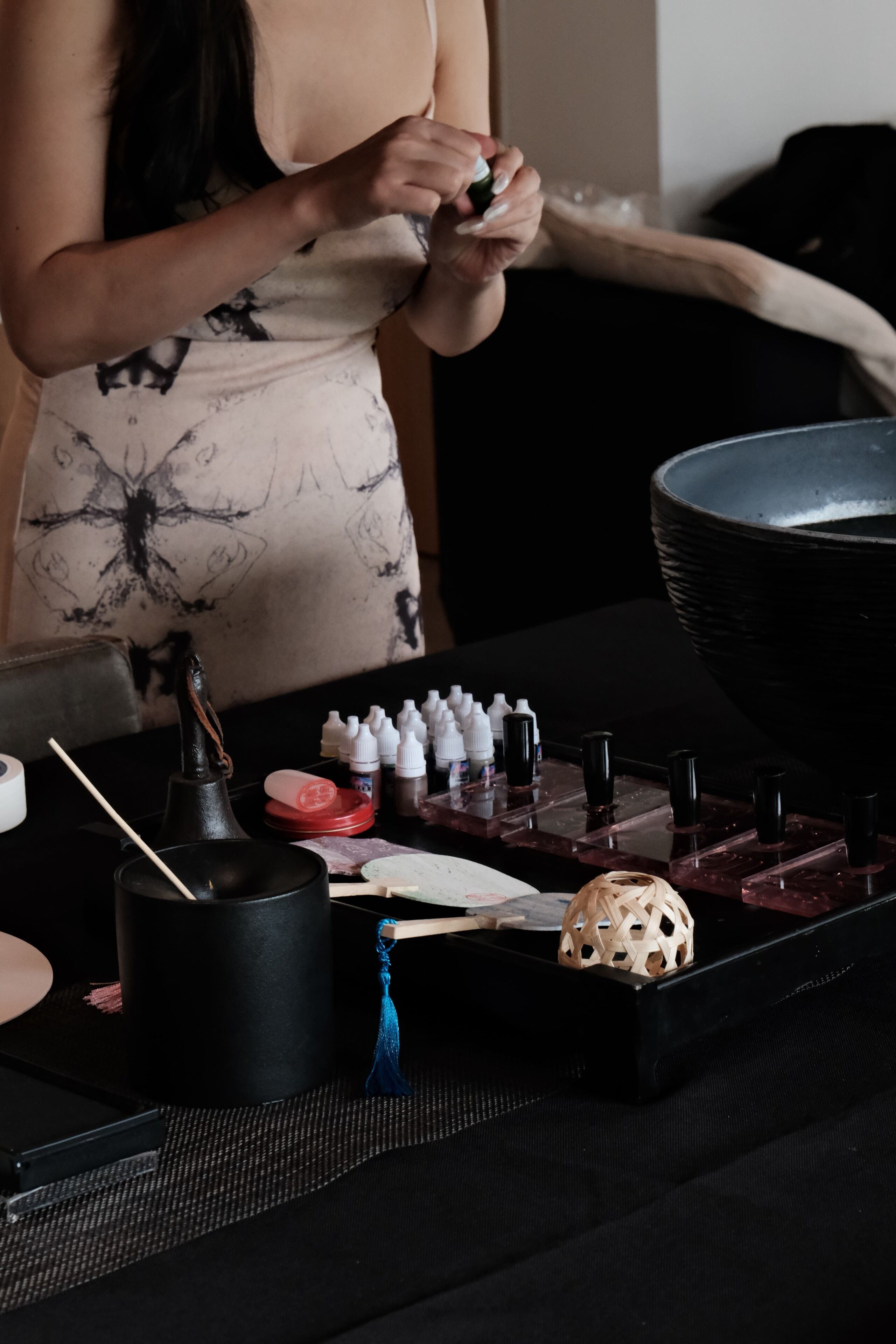 Une personne est en train de jouer à un jeu de société sur une table. Le jeu se déroule sur un plateau noir et rouge, et on peut voir un bol noir ainsi que diverses petites bouteilles sur la table.