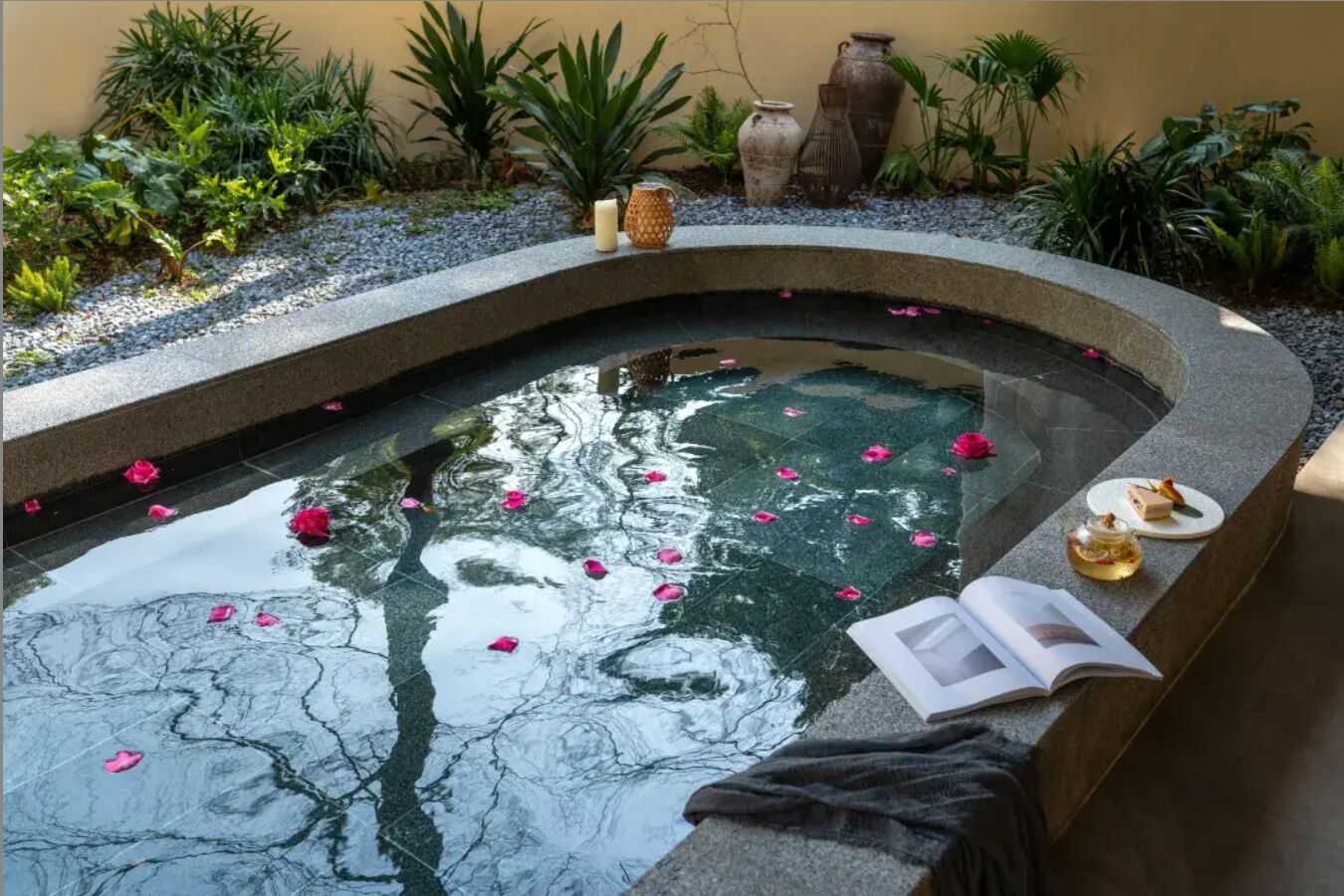 A serene indoor pool with a curved edge, surrounded by various plants and decorative vases.