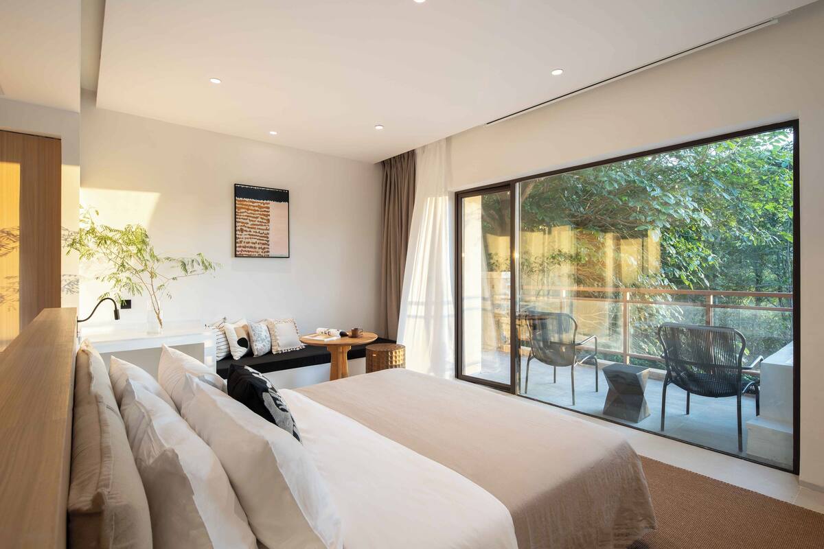A modern hotel room with a large bed, a small table, and a balcony with chairs.