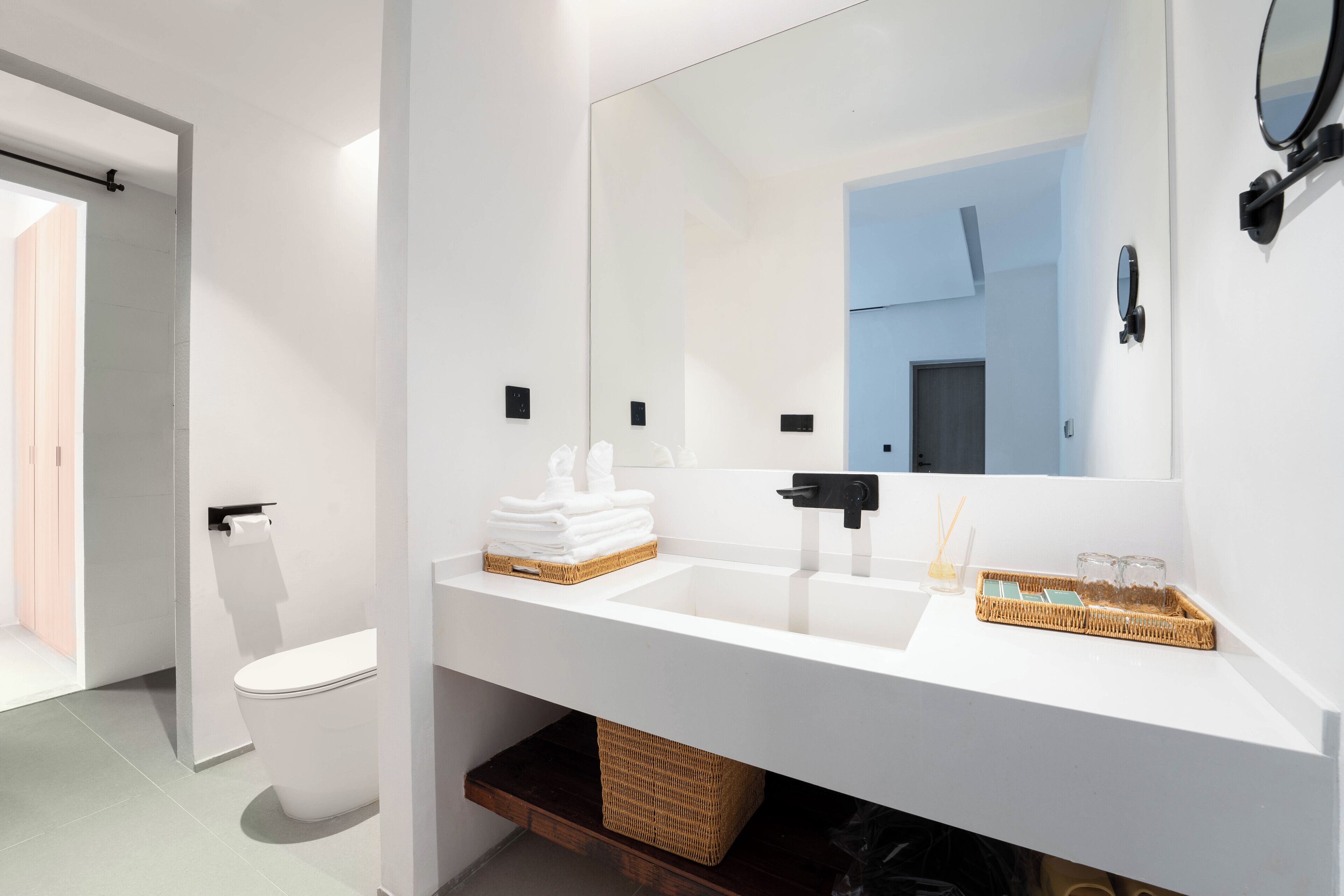 A modern bathroom with a white sink, a large mirror, and a toilet.