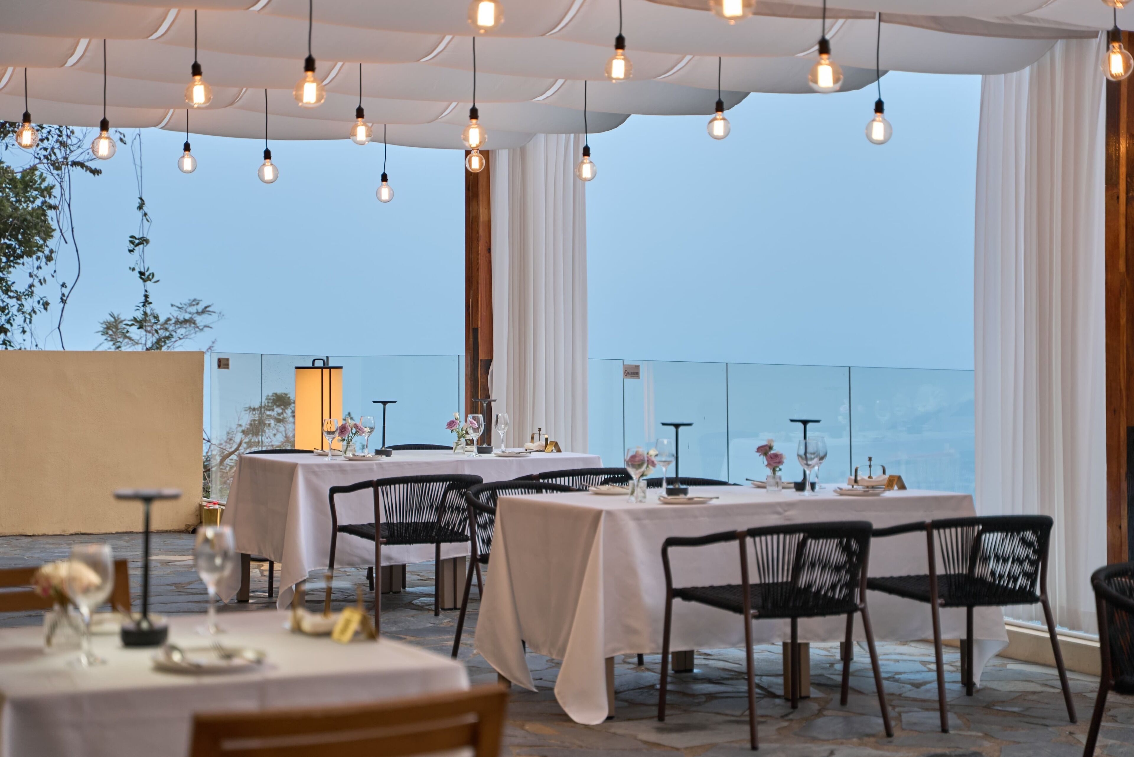 Un restaurant où les tables sont dressées pour le service, offrant une vue sur la mer.