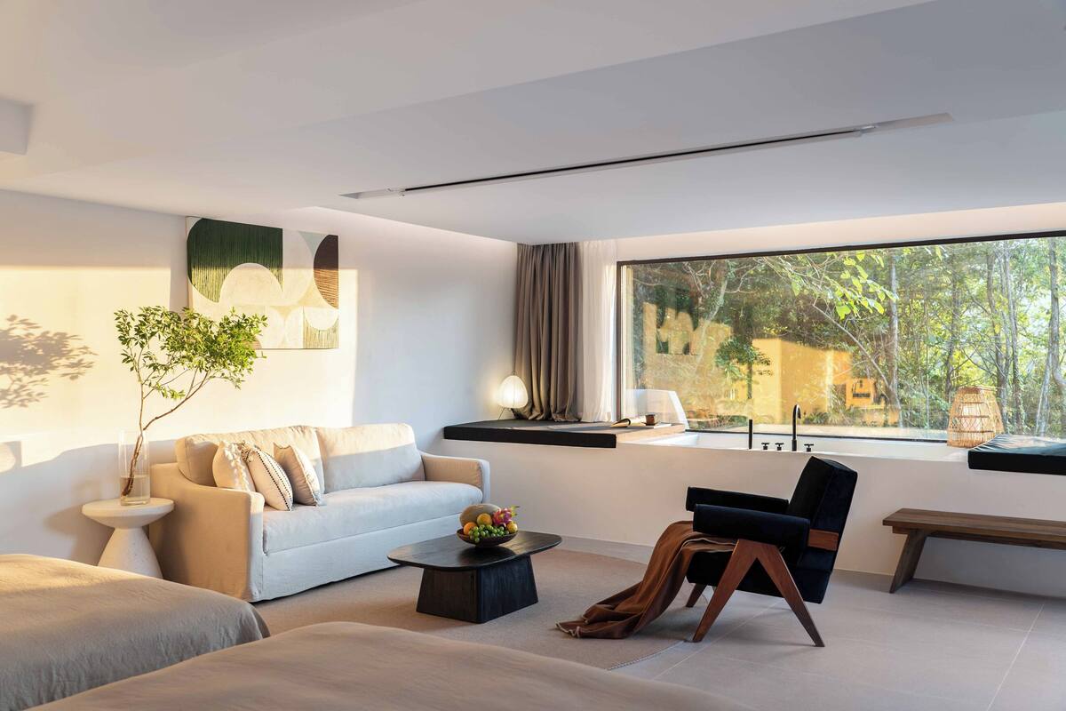 A modern living room with a sofa, a black chair, a coffee table, and a large window with a view of trees and buildings.