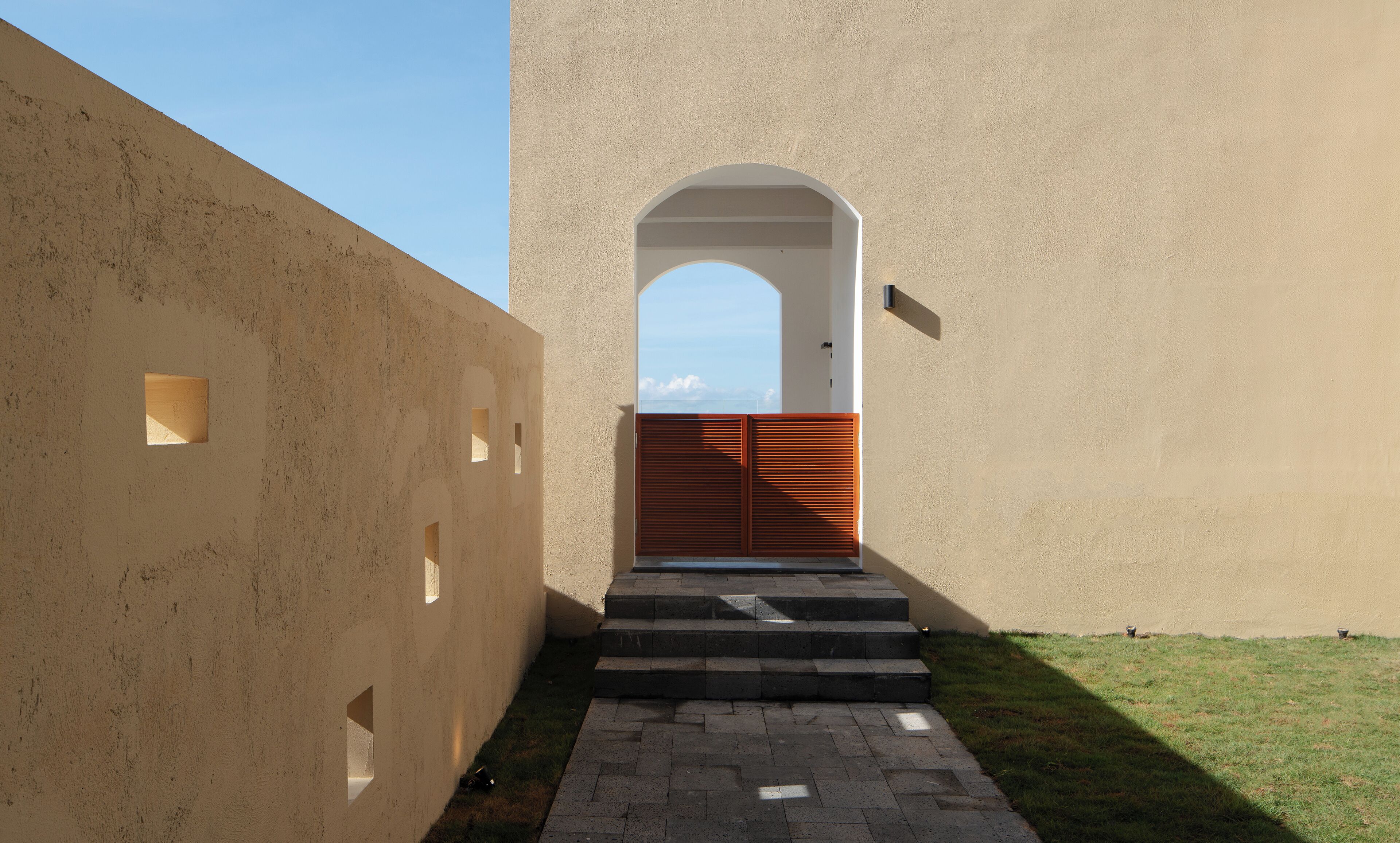 A building with a beige exterior, a wooden door, and a set of steps leading to an arched entrance.