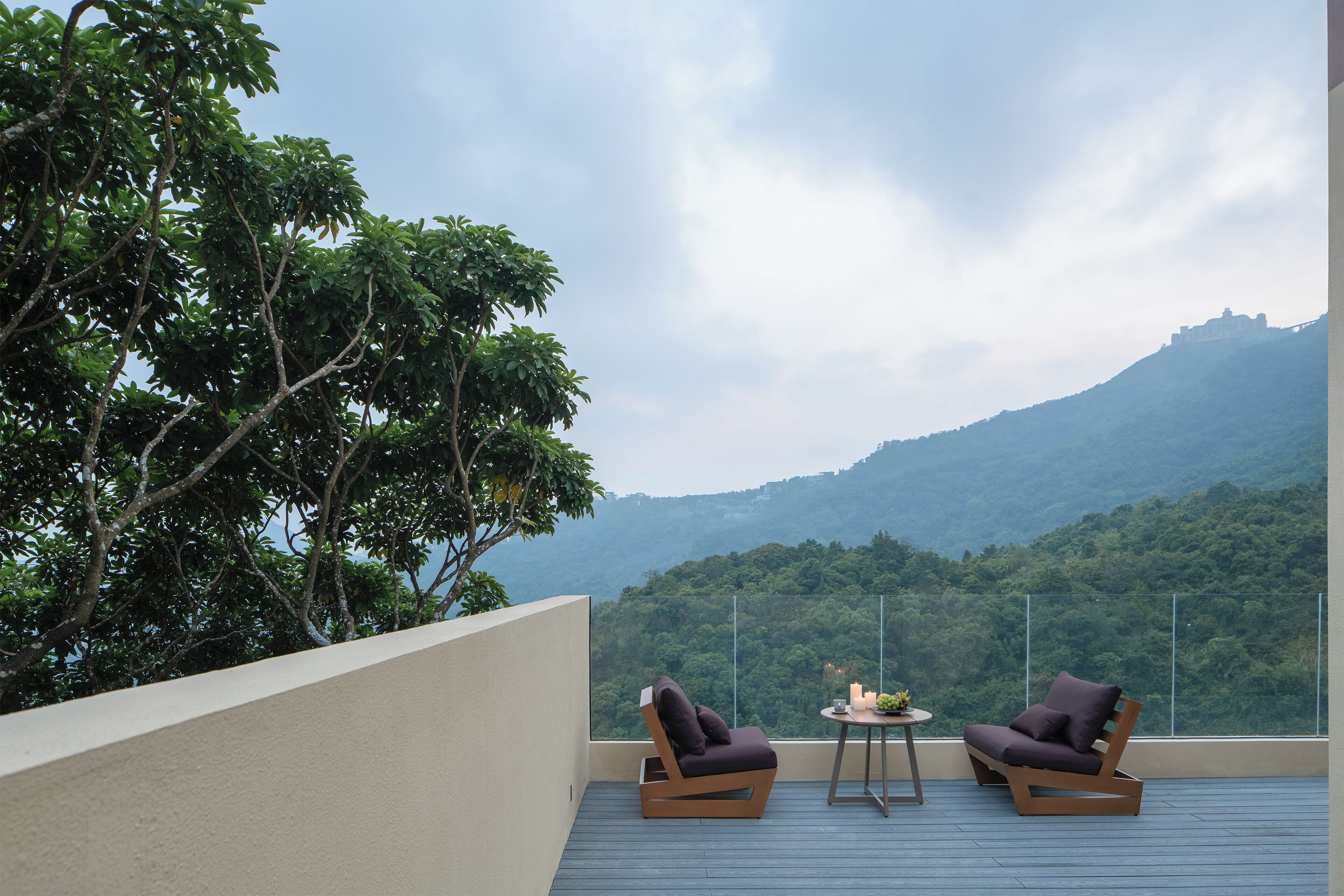 A balcony with two chairs and a small table, overlooking a mountainous landscape.