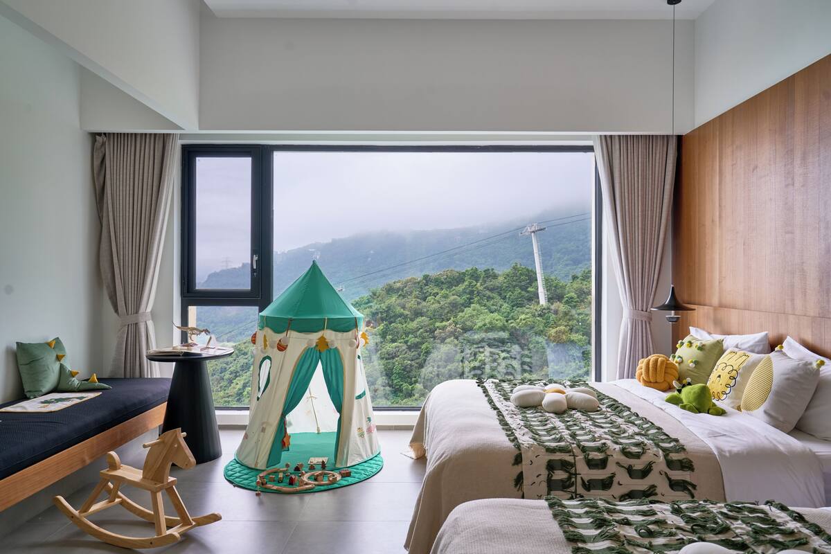 A bedroom with a bed, a rocking chair, a tent, and a view of a forested area.