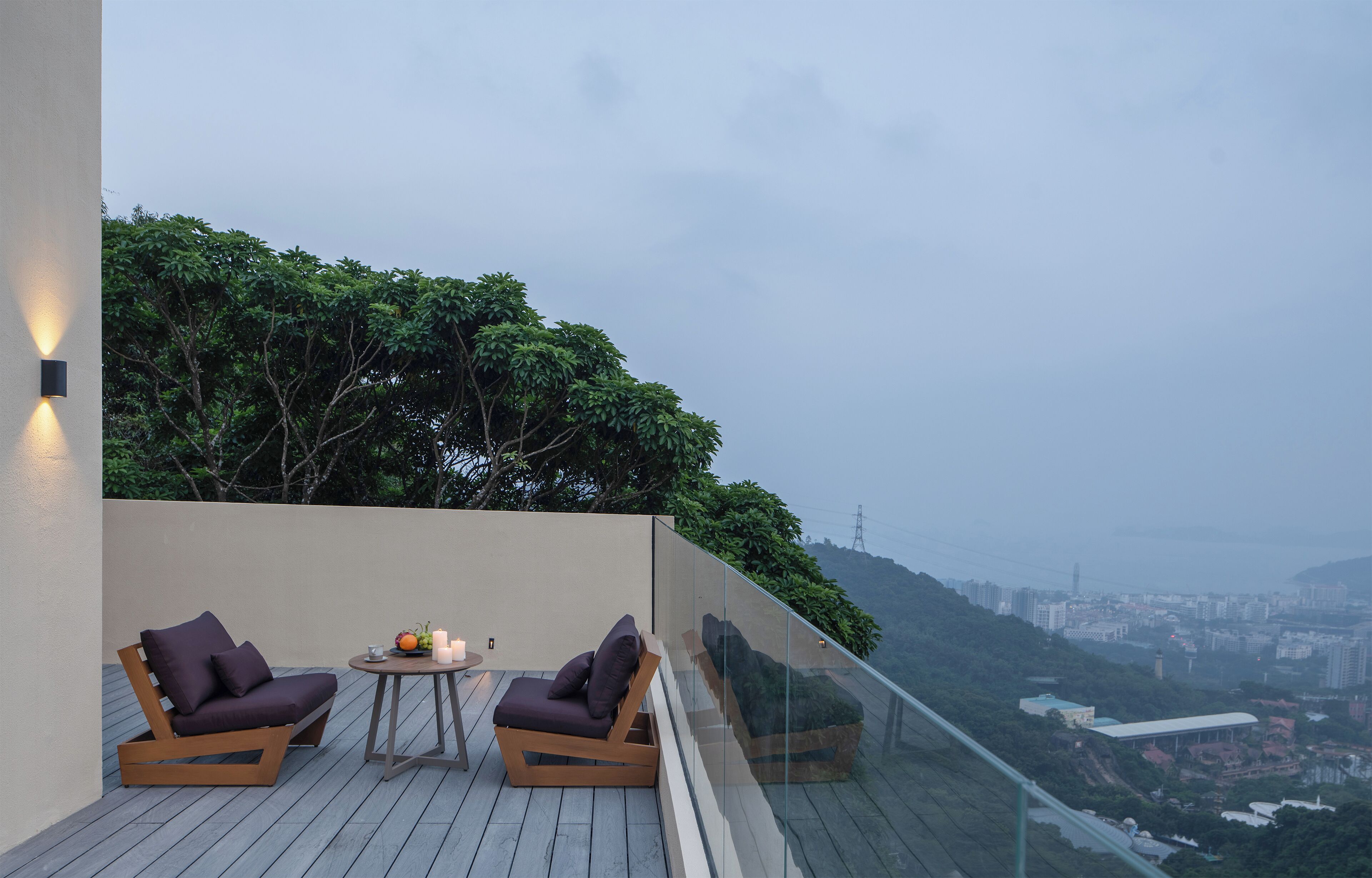Un balcon avec deux fauteuils confortables et une petite table sur laquelle est posée une bougie, offrant une vue sur le paysage urbain et la verdure.