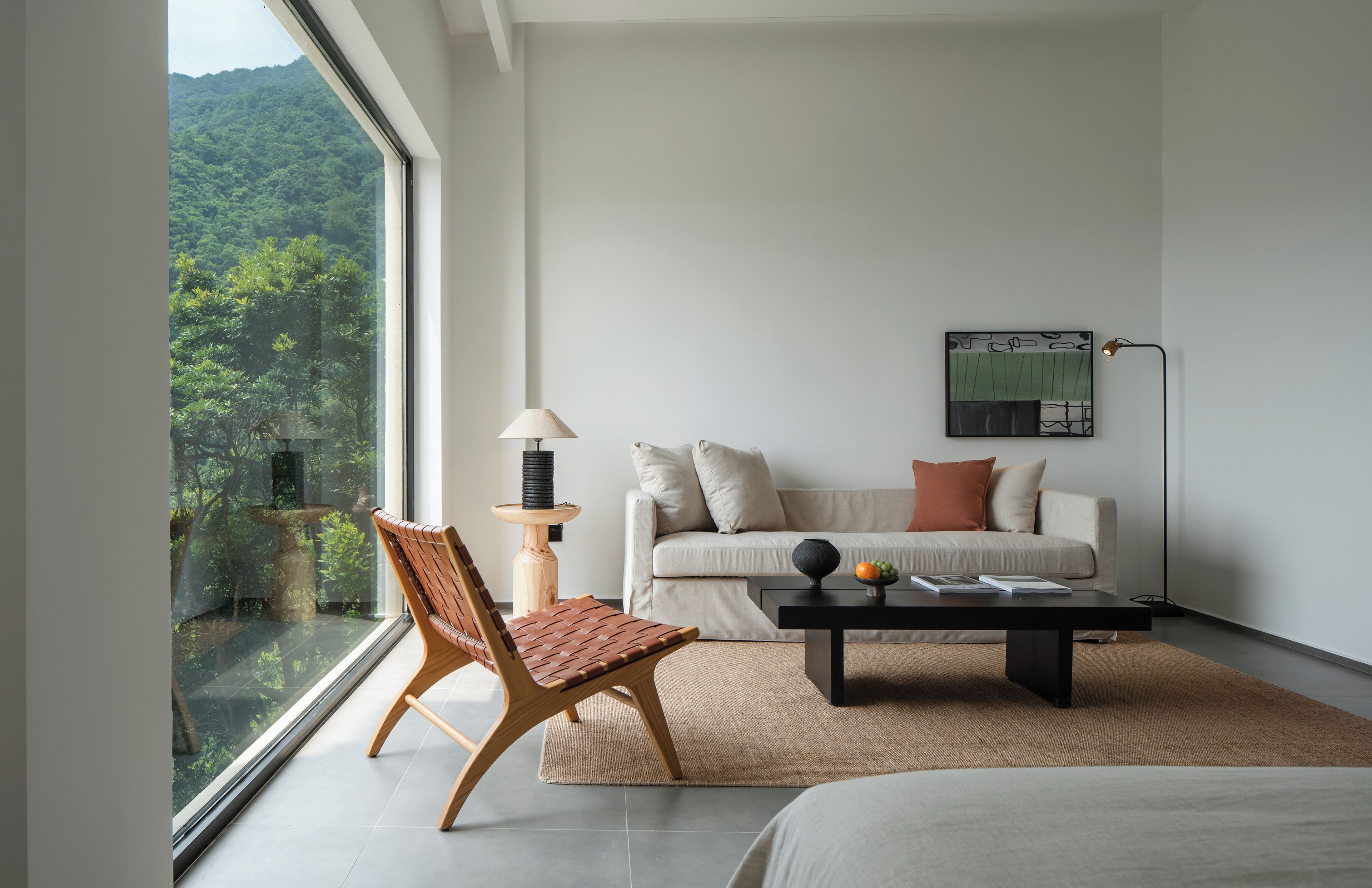 Una sala moderna con un sofá, una mesa de centro y una silla. Una ventana grande ofrece vistas a un área boscosa.